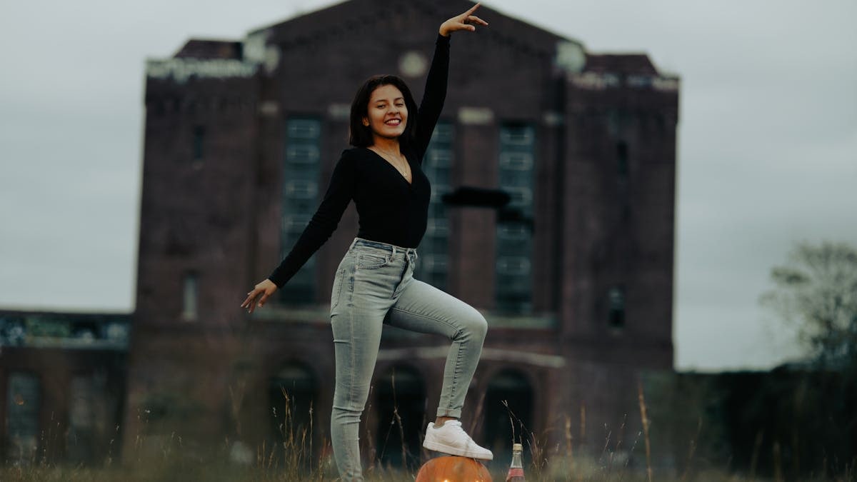 A woman poses with a carved pumpkin in front of an abandoned building, celebrating Halloween.