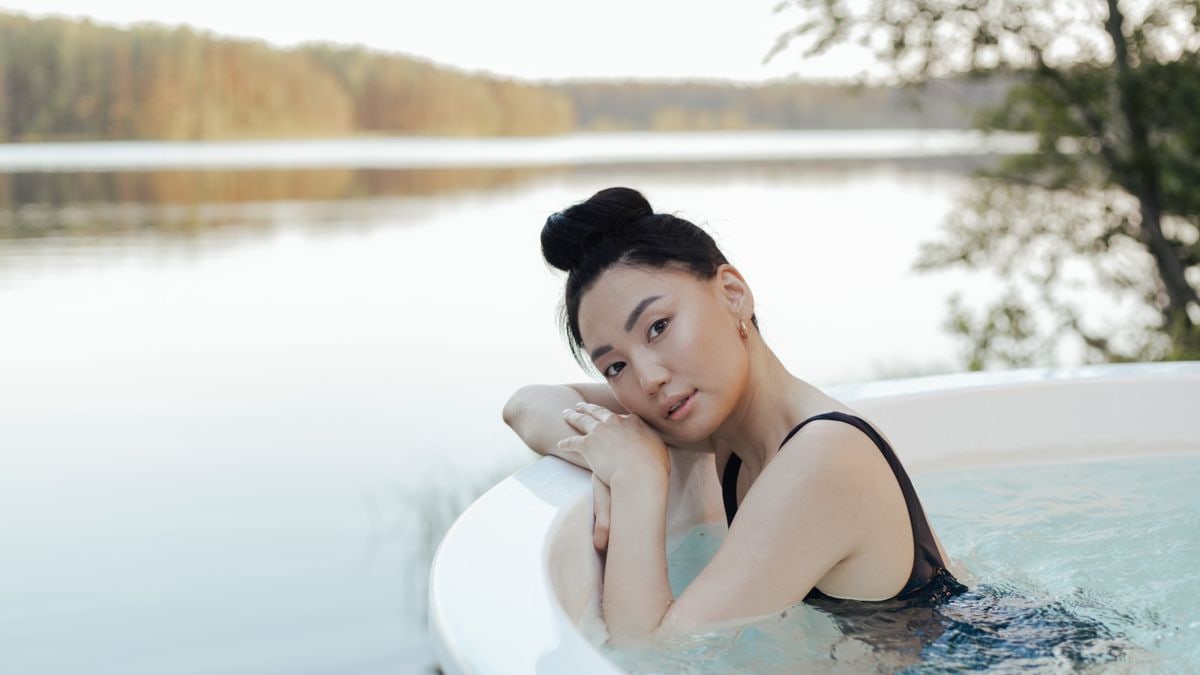 A woman enjoys a relaxing time in an outdoor hot tub by a serene lakeside setting.